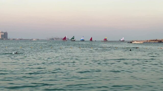 People are swimming in the sea and old lenj traditional Qatar boat are sailing in a pink blue back ground of twilight after sunset in FIFA world cup Qatar 2022 event ceremony tournament Match games