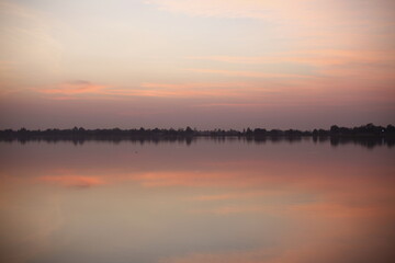 Scenic view of beautiful sunrise or dawn above the pond at spring or early summer morning with cloudy sky background and fog over water. Landscape. Water reflection.