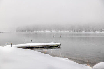 Snow cover pier on a lake on foggy day