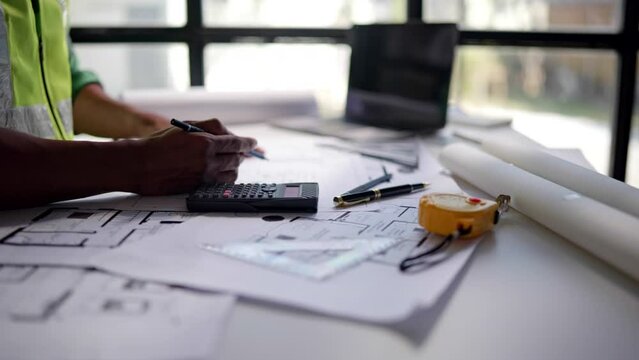 Close up of hands working and calculations estimate for cost and materials planning on paperworks and floor plan drawings about design architectural and engineering for houses and buildings.