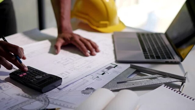 Close up of hands working and calculations estimate for cost and materials planning on paperworks and floor plan drawings about design architectural and engineering for houses and buildings.