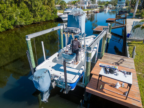 Tower boat with covers on boat lift with deck dock with person on board in Tampa Florida from aerial drone