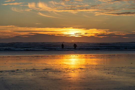 Two surfers in silhouette wading into the surf at sunset