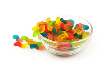 Many colorful worm shaped gummy candies escaping from glass bowl isolated on white background.