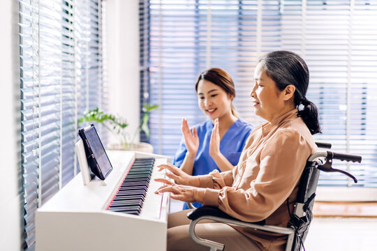 Portrait of asian nurse physiotherapist carer helping smiling and having fun teaching and play piano music lesson with asian senior elderly woman at home visit.senior retirement care concept