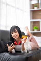 Asian woman using credit card and mobile phone for online shopping At home while lying on the phone for online shopping and online payment concept with credit card