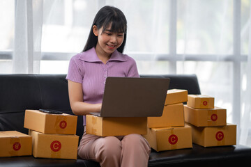 Asian women working SME business at the workplace at home. use laptop to check customer orders online shipping boxes, freelance SME entrepreneur online business idea.