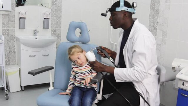 A young girl at a medical examination or examination in the office of an otolaryngologist is an African-American doctor. Earwash and removal of earwax