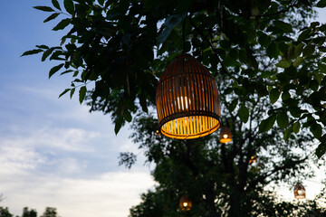 Bamboo lamps are lit by orange light bulbs hanging from the trees at sunset.