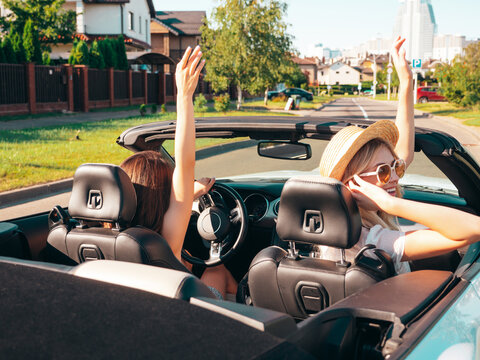 Portrait of two young beautiful and smiling hipster female in convertible car. Sexy carefree women driving. Positive models riding and having fun in sunglasses outdoors. Enjoying summer days