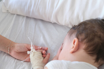 sick toddler in hospital holding mother's hand while sleeping