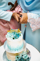 Bride and a groom is cutting their wedding cake on wedding banquet. Hands cut the cake with delicate blue flowers.