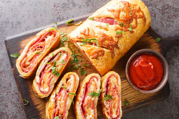 Italian food Pizza roll stromboli with cheese, salami and tomatoes closeup on the wooden board on the table. Horizontal top view from above