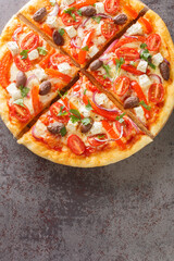 Fresh Homemade Vegetarian Greek Pizza with feta and vegetables closeup on the wooden board on the table. Vertical top view from above