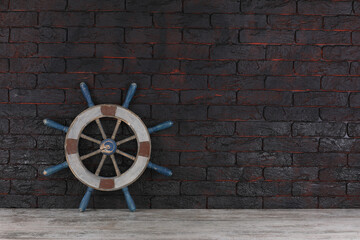 ship steering wheel on a black brick wall © serikbaib