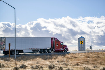 Dark red big rig classic American semi truck tractor transporting cargo in refrigerator semi...