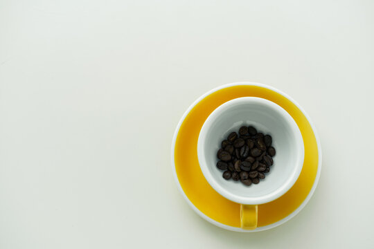 A yellow cup with coffee beans in it, on a white background.
