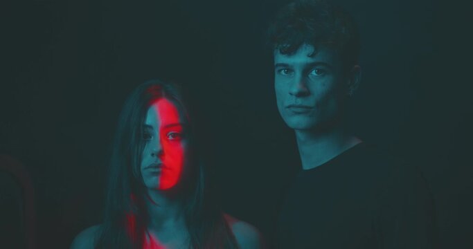 Man and woman look toward camera in a teal and ted light