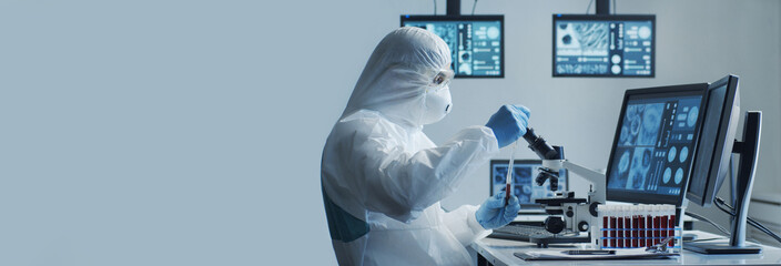 Scientist in protection suit and masks working in research lab using laboratory equipment:...