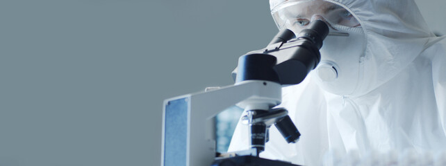 Scientist in protection suit and masks working in research lab using laboratory equipment: microscopes, test tubes. Coronavirus 2019-ncov hazard, pharmaceutical discovery, bacteriology and virology.