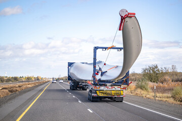 Fototapeta Powerful big rig semi truck with additional axle dolly with oversize load sign transporting wind turbine blade running on the straight highway road obraz