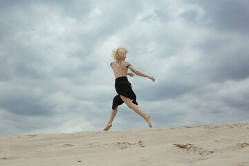 Fototapeta premium Elegant bare woman jumping on beach scenic photography. Picture of person with overcast sky on background. High quality wallpaper. Photo concept for ads, travel blog, magazine, article