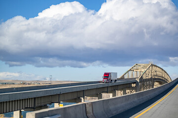Red big rig semi truck transporting frozen cargo in reefer semi trailer driving on the overpass...