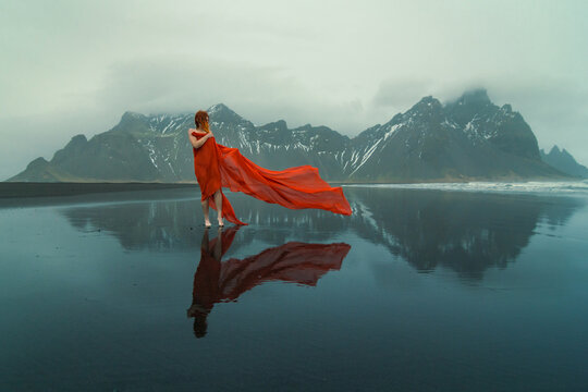 Lady wrapped with red fabric on Reynisfjara beach scenic photography. Picture of person with hills on background. High quality wallpaper. Photo concept for ads, travel blog, magazine, article