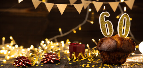 Number 60 golden festive burning candles in a cake, wooden holiday background. sixty years of...
