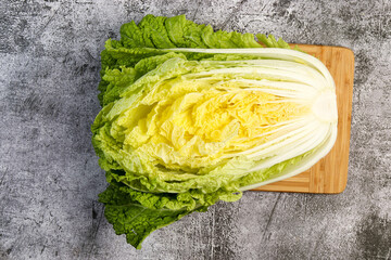 Half head of Napa Chinese cabbage on a wooden cutting board on a dark grey background. Top view,...