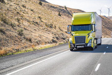 Fototapeta na wymiar Successful big rig yellow semi truck transporting cargo in refrigerator semi trailer driving uphill on the wide highway road