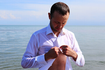 a handsome man is buttoning up a wet white shirt