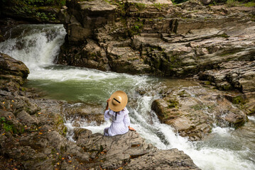 A girl sitting on the stone among the mountains and looking at the river. Woman sits near the mountain river enjoy the view. The rapids on the river.
