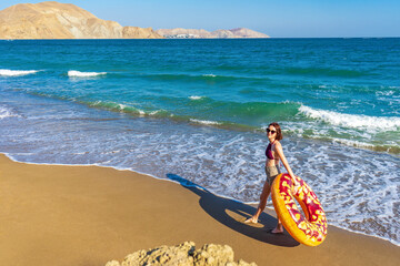 Teen girl with donut lilo against summer landscape of sea and mountains on sunny day. Beautiful...