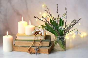 Bouquet of Snowdrop flowers with willow branches, christian rosary beads, books and candles on...