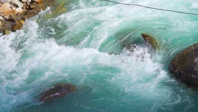 Slow motion shot of river Parvati flowing rapidly at Kasol in Himachal Pradesh, India. Clear blue colored river running in between the Himalayan mountains in India. Natural Himalayan river background.