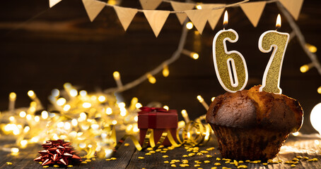 Number 67 golden festive burning candles in a cake, wooden holiday background. sixty-seven years of birth. the concept of celebrating a birthday, anniversary, holiday. Banner.