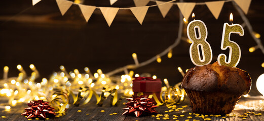 Number 85 golden festive burning candles in a cake, wooden holiday background. Eighty-five years...