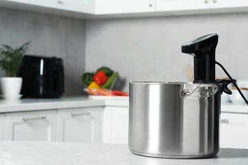 Pot with sous vide cooker on table in kitchen, space for text. Thermal immersion circulator
