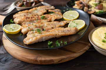 Pan fried fish with creamy polenta and mushrooms fried in butter on a rustic and wooden table for dinner or lunch