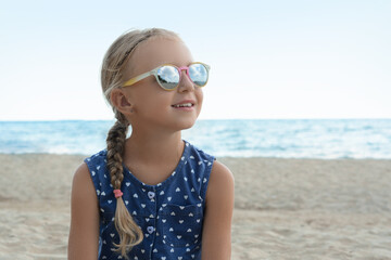 Little girl wearing sunglasses at beach on sunny day. Space for text
