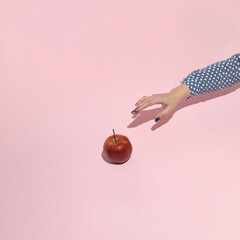 Female hand reaching for fresh apple on pink background. Minimal concept.