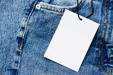 Fashion background with empty copy space. Blank white paper label tag. Blue jeans denim texture with thread sew lines. Brown clothing tag. Black friday clothes sale. Price tag on a string.