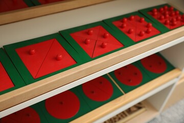 Wooden puzzles with different geometric shapes on shelves in room, closeup. Montessori toy - obrazy, fototapety, plakaty