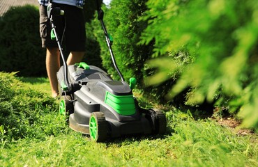 Man cutting grass with lawn mower in garden on sunny day, closeup