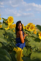 A beautiful Ukrainian girl, standing in a field of sunflowers, wrapped in her national flag, the flag of Ukraine. No war in Ukraine
