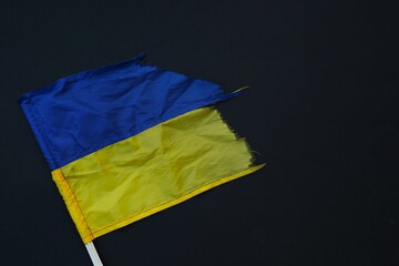 Torn, shabby Ukrainian flag, lies on a black background, no war in Ukraine