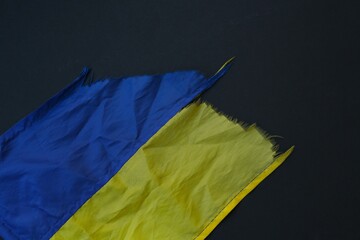 Torn, shabby Ukrainian flag, lies on a black background, no war in Ukraine