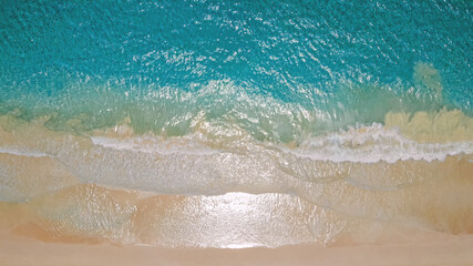 Tropical beach top view, waves break on tropical white sand beach top view. Wave roll into beach with white clean foam. Summer sunset seascape. Top view beach sea. Sunny day at seaside