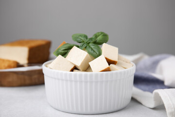 Bowl of smoked tofu cubes with basil on white table, closeup